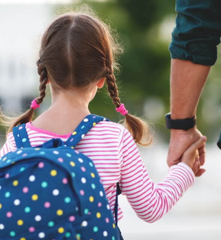 a dad walking his daughter to school holding her hand
